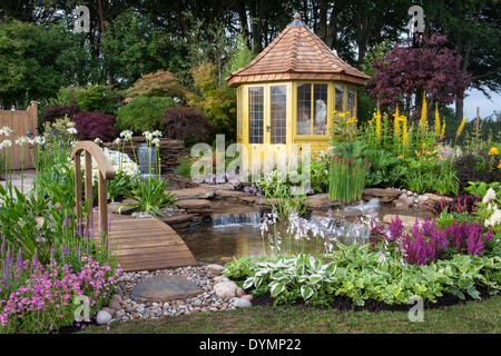 Cottage di campagna inglese giardino estivo con ponte casetta estiva casetta estiva piccolo laghetto d'acqua caratteristica cascata un misto colorato confine fiorito Regno Unito Foto Stock