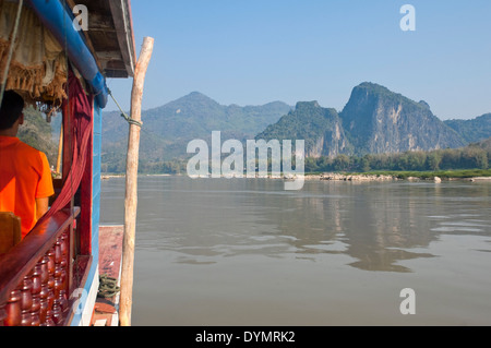 Ritratto orizzontale di un uomo laotiano captaining una barca lenta fino il fiume Mekong in una giornata di sole. Foto Stock