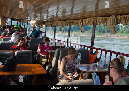 Vista orizzontale di turisti occidentali che viaggiano fino il fiume Mekong in un laotiano barca lenta. Foto Stock