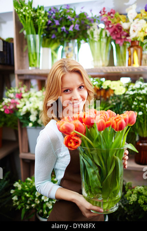 Ritratto di giovane donna fioraio con grande vaso di tulipani rossi guardando la fotocamera Foto Stock