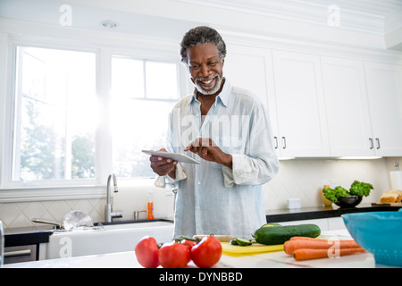 Senior uomo con tavoletta digitale in cucina Foto Stock