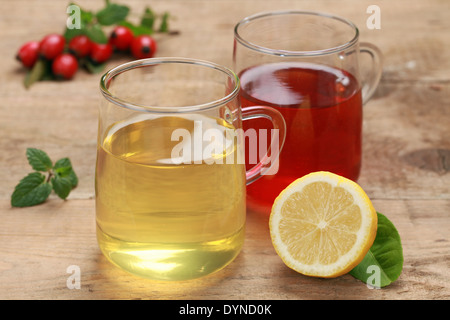 Il rosso e il giallo da tè di limoni e di rosa canina in bicchieri su una tavola di legno Foto Stock
