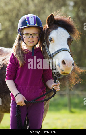 Una giovane ragazza in piedi con un pony al di fuori in campagna in una giornata di sole e sorridente alla fotocamera Foto Stock