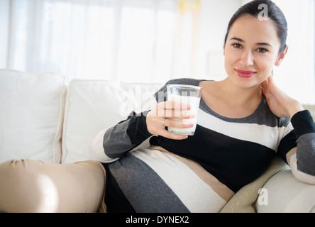 Incinta donna caucasica bere latte sul divano Foto Stock