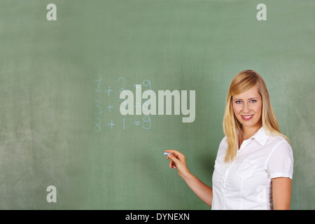 Insegnante di matematica di scrittura problema su una lavagna nella scuola elementare Foto Stock