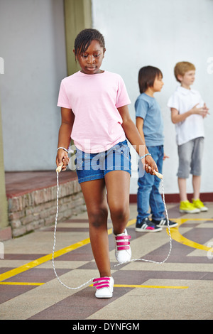 La ragazza del salto con la corda da salto su schoolyard nella scuola elementare Foto Stock