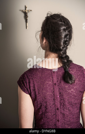 Vista posteriore della donna che guarda al crocefisso appeso alla parete Foto Stock