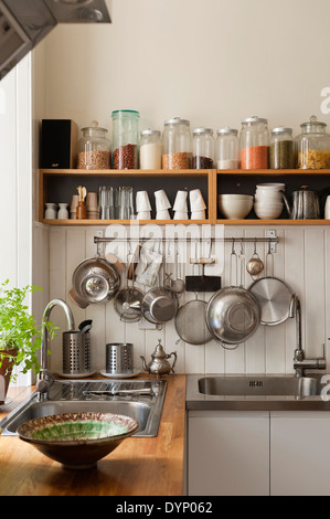 Gli ingredienti secchi su scaffali aperti e gli utensili appesi da una padella in rack angolo cottura con lavandini e rovere massiccio delle superfici di lavoro Foto Stock