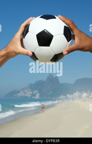 Il brasiliano interracial mani tenendo il calcio al di sopra di due fratelli di montagna la spiaggia di Ipanema di Rio de Janeiro in Brasile Foto Stock