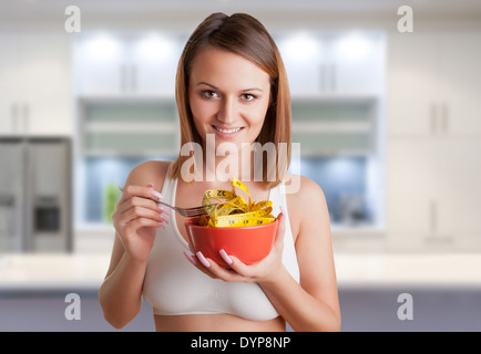 Concetto di immagine di una donna su una dieta mangiando un nastro di misurazione, in una cucina Foto Stock