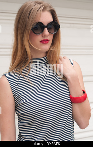 Un capelli biondi donna, caucasico modello femminile che indossa un 60s abito, round occhiali da sole, stripe top, 60s di moda vintage concept Foto Stock