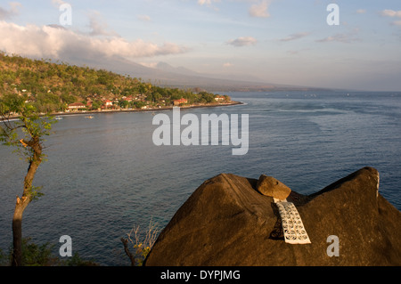 Una preghiera su di una roccia che si affaccia il piccolo villaggio di pescatori di Amed, con Gunung Agung mountain sullo sfondo (3142m). A est di Bali. Amed Foto Stock