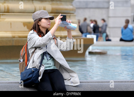 Londra, Inghilterra, Regno Unito. Giovane donna giapponese in tappata ha raggiunto il picco di scattare una foto sul suo telefono cellulare in Trafalgar Square Foto Stock