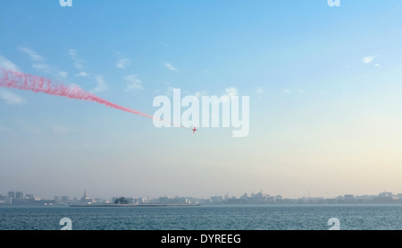 Una freccia rossa piano fa fumo che vola al di sopra della Baia di Doha, Qatar, con punti di riferimento come il Emiri Diwan palace all'orizzonte Foto Stock