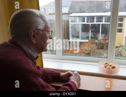 Lonely vecchio uomo guardando fuori della finestra sul giardino a. Foto Stock