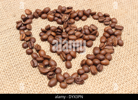 Vista dettagliata del cuore a forma di chicchi di caffè, Valentino cuore di caffè, caffè in chicchi su sfondo di iuta Foto Stock