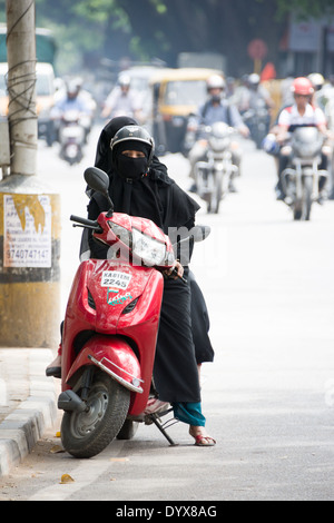 Un elegante donna che indossa un velo niqab, seduta sul suo scooter con un amico mentre guardando freddamente nella fotocamera. Foto Stock