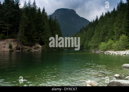 Vista di aqua-verde ingresso tranquilla circondata da una foresta con grandi alta montagna nebbioso in background Vancouver Foto Stock