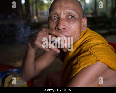 Cambogiano monaco buddista di fumare un sigaro handrolled realizzato con foglia sankai, accanto al tempio Bayon, Angkor Thom, Siem Reap, Cambogia Foto Stock