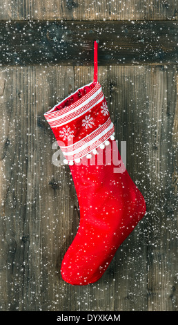 Calza rossa con i fiocchi di neve per Santa regali appesi sopra in legno rustico sfondo. Calza di Natale. Foto Stock