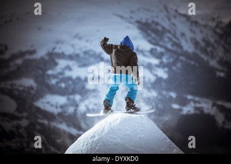 Snowboarder indossa una felpa con cappuccio, gira su una cupola di neve con le montagne sullo sfondo. Foto Stock