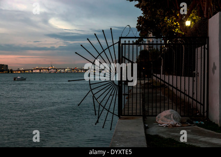 Persona senzatetto dorme in modo irregolare a sunrise lungo il seawall su Biscayne Bay a Miami, Florida, Stati Uniti d'America. Foto Stock