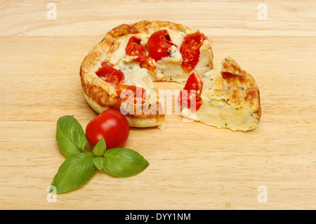 Pomodoro, basilico e mozzarella quiche su una tavola di legno con una fetta tagliata e un ciuffo di basilico e un pomodoro Foto Stock