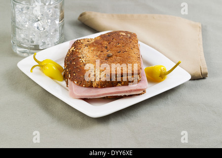 La foto in orizzontale del panino di prosciutto fatto con grano intero pane sulla piastra bianca con peperoni gialli e bicchiere di acqua in background Foto Stock