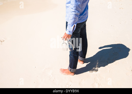 Primo piano di due wineglasses in una mano d'uomo sulla spiaggia di sabbia bianca Foto Stock