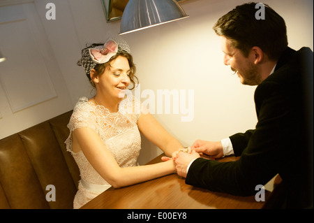 Felice sposa e lo sposo tenere le mani su un tavolo nella sala da pranzo sia a un matrimonio vintage Foto Stock