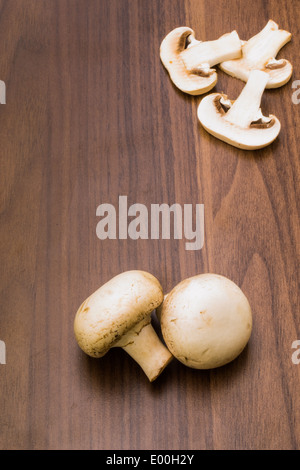 Due pulsanti/funghi champignon su uno sfondo marrone con tre fette di fungo nell'angolo in alto a destra. Foto Stock