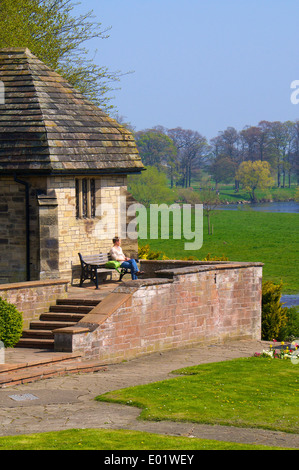 Donna seduta su una panchina in un edificio monumento. Fumare una sigaretta ascoltando musica con in-ear telefoni di testa. Foto Stock