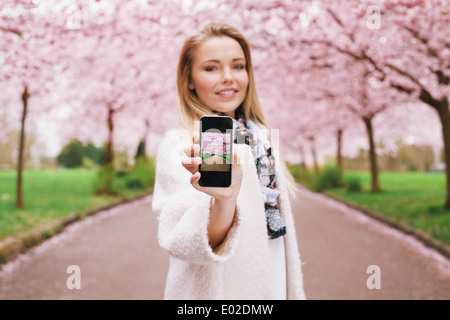 Piuttosto giovane donna mostra un'immagine della molla blossom garden mentre si sta in piedi in un parco. Caucasian giovani femmine che mostra la molla park Foto Stock