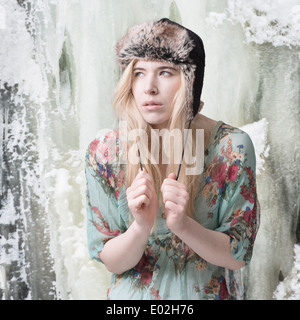 Donna bionda nella parte anteriore del ghiaccio coperto mountain indossando abiti estivi e invernali hat Foto Stock