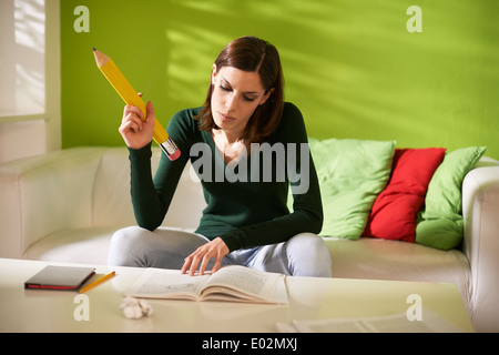 Giovane studente caucasica facendo homeworks e prendere appunti sul libro con enorme matita a casa Foto Stock