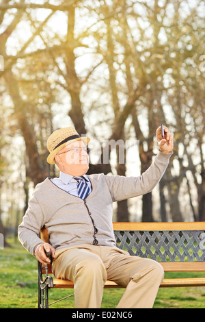 Un vecchio uomo prendendo un selfie con telefono cellulare seduti sul banco di prova all'aperto Foto Stock