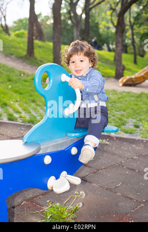 Curly ragazzo su altalena nel parco con alberi in background Foto Stock