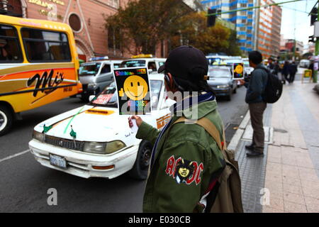 LA PAZ, Bolivia, 30 aprile 2014. Uno studente con un AC/DC 'autostrada all'inferno" badge sulla sua giacca detiene una targhetta durante n. Avvisatore acustico giorno / Dia de la No Bocina, una campagna per incoraggiare i driver per utilizzare il loro corno inferiore e a ridurre l' inquinamento acustico in città. La Paz è famosa per il suo traffico caotico; il Municipio corre frequentemente le campagne in materia di sicurezza stradale e a ridurre la congestione e simili. Credito: James Brunker / Alamy Live News Foto Stock