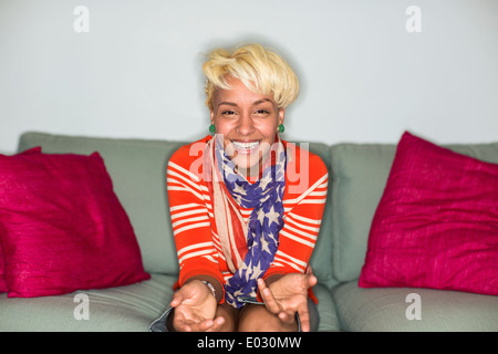 Una donna con capelli biondi seduta su un divano con un sorriso. Foto Stock