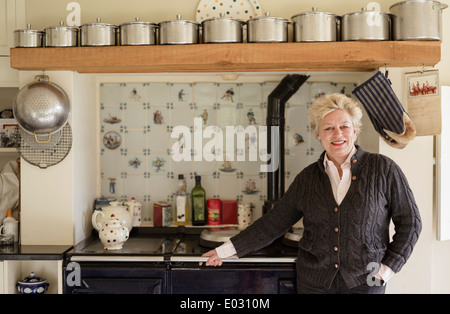 Una donna in piedi con la schiena di un fornello nella sua cucina. Foto Stock