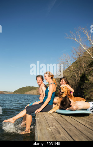 Una famiglia e il loro cane recuperatore su un molo da un lago. Foto Stock