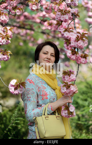 La fioritura dei ciliegi nel giardino e una donna in abiti colorati e foulard giallo Foto Stock