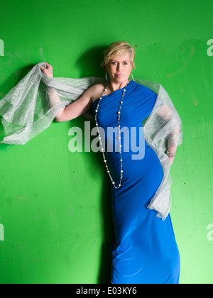 Donna matura indossando abiti blu e in posa, verde parete in calcestruzzo su sfondo Foto Stock
