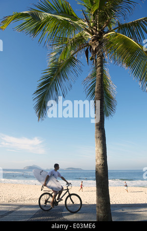 RIO DE JANEIRO, Brasile - 21 febbraio 2014: uomo cavalca una bicicletta che trasportano le tavole da surf lungo la passerella a Arpoador lungo una vista Foto Stock