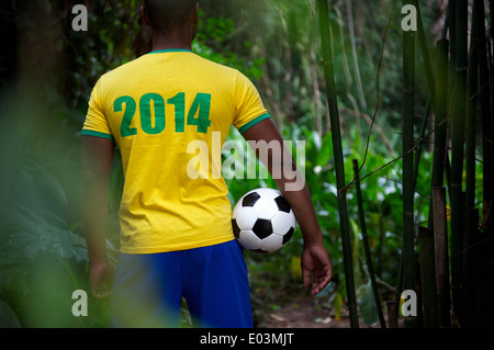 Il calcio brasiliano giocatore nel 2014 shirt in piedi in bambù giungla tropicale tenendo palla calcio Foto Stock