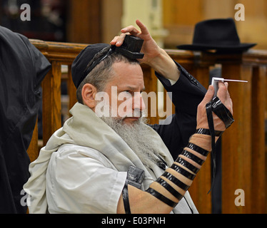 Usando uno specchio una religiosa ebraica uomo regola il suo phylacteries presso le preghiere del mattino a Lubavitch sede a Brooklyn, NY Foto Stock