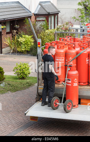 Un uomo di consegna Consegna famiglia red Calor Gas bottiglie su un pickup carrello elevatore di coda al di fuori di una struttura interna. Regno Unito, Gran Bretagna. Foto Stock
