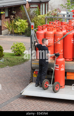 Un uomo di consegna Consegna famiglia red Calor Gas bottiglie su un pickup carrello elevatore di coda al di fuori di una casa. Il Galles del Nord, Regno Unito, Gran Bretagna Foto Stock