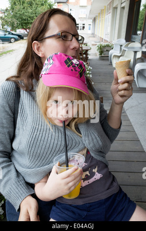 Figlia di peperoncino avvolto all'interno di MOM's maglione sorseggiando il suo succo di arancia attraverso una paglia con età di 6 e 34. Rawa Mazowiecka Polonia centrale Foto Stock