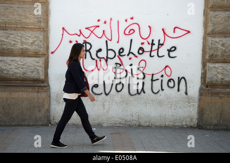 Tunisia 2014. Una donna che indossa jeans passeggiate passato slogan dicendo rivoluzione scritto su una parete Foto Stock